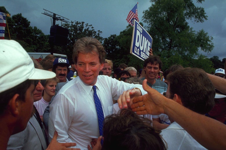 David Duke shakes hands with supporters who are surround him. A "David Duke U.S. Senate" sign can be seen farther back.