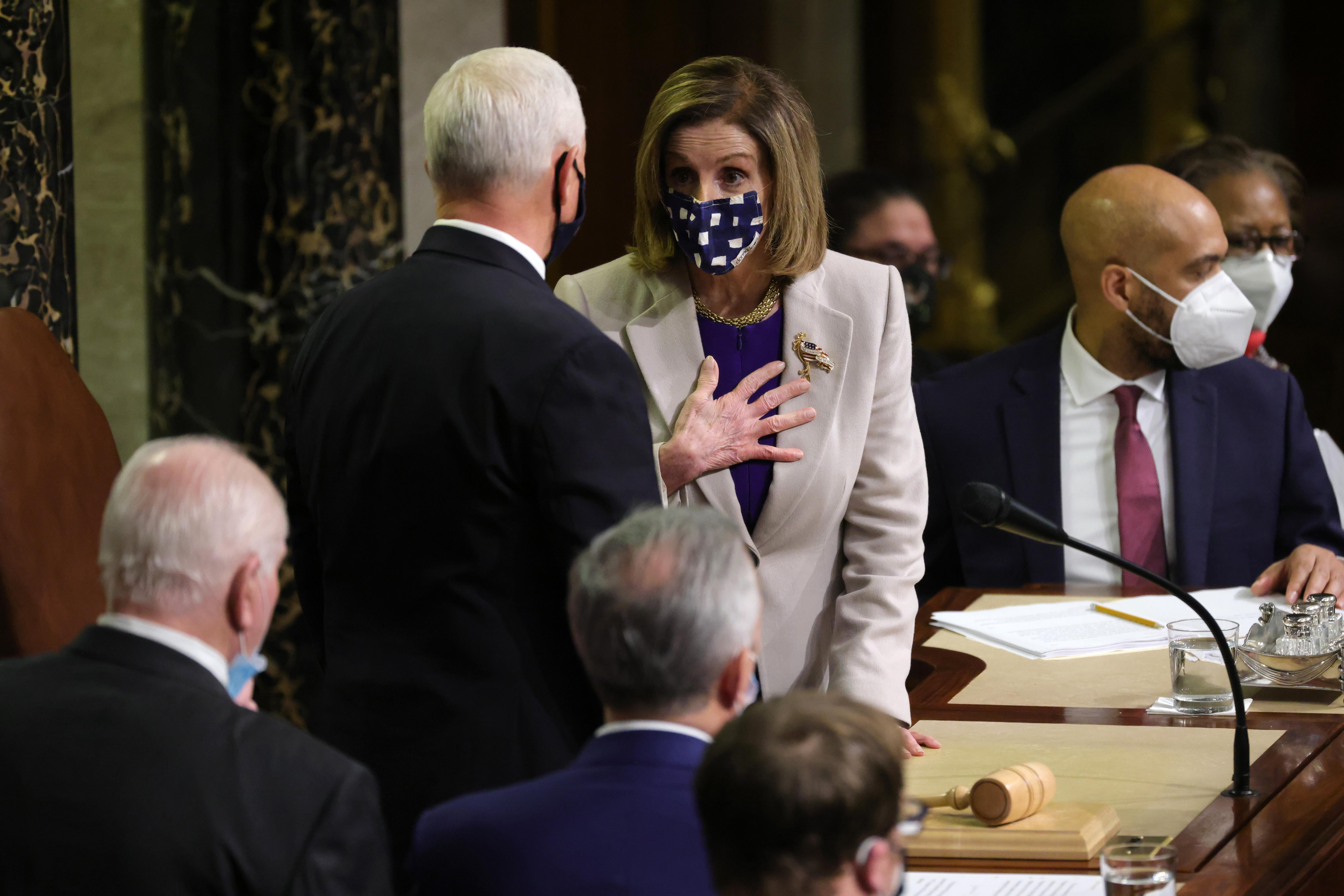 Mike Pence talks to Nancy Pelosi, both standing at the rostrum of the House chamber surrounded by other people