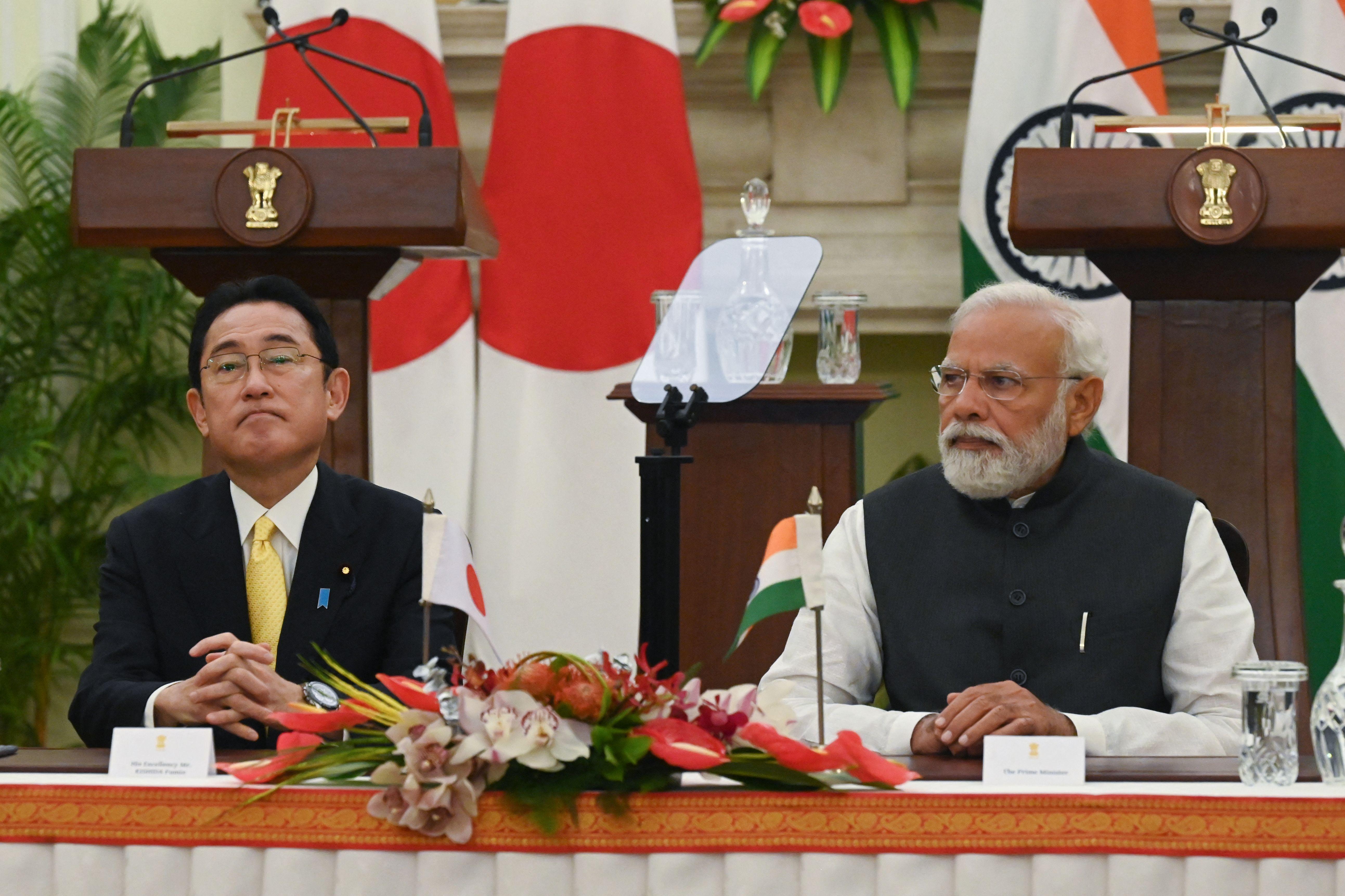 Kishida and Modi sit at a table with flowers and little flags of Japan and India in front of them.