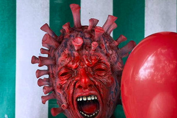 Someone wearing a latex scary coronavirus mask, next to a red balloon and against a green-and-white striped background.