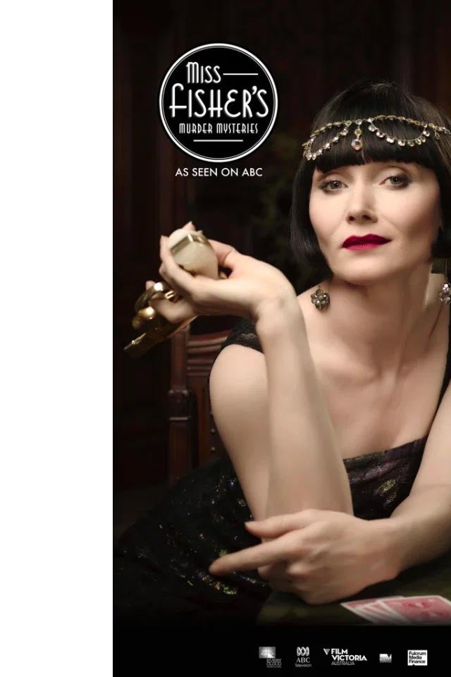 Essie Davis, her hair in a blunt black bob, leans on a table with playing cards on it.