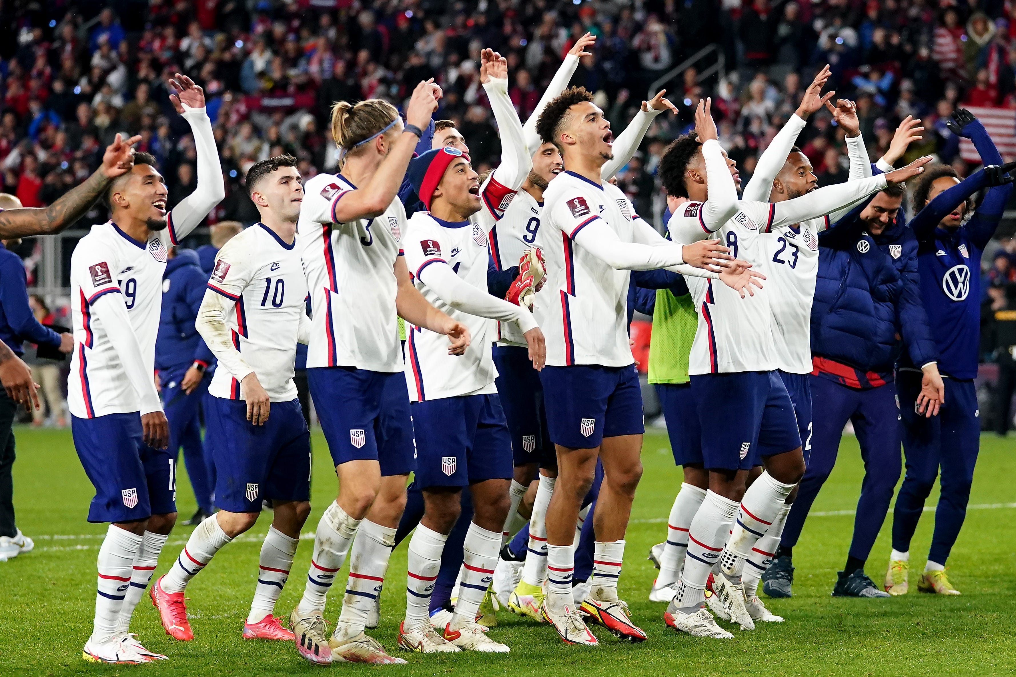 The U.S. men's soccer team waves their arms and cheers toward the crowd, on the pitch together after beating Mexico.
