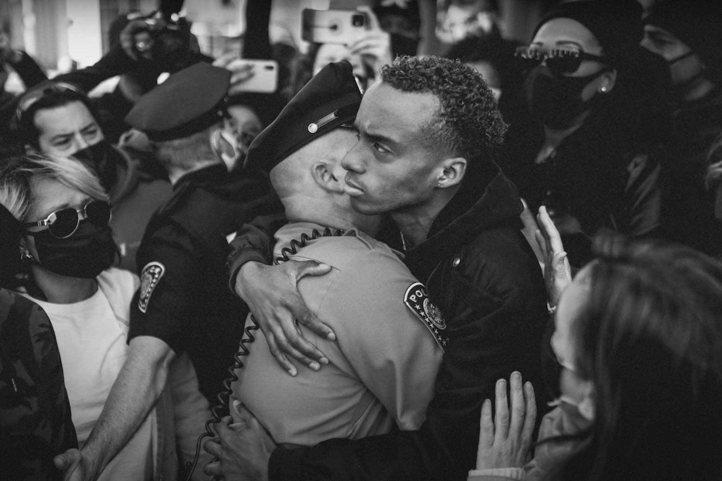A young black man hugs a white police officer in a crowd.