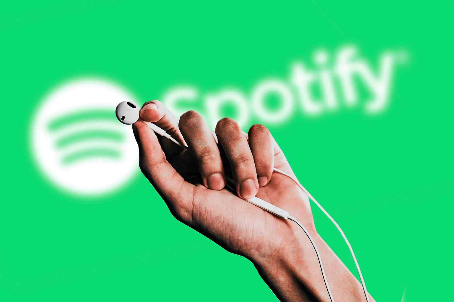 Hand holding wired Apple earphones in front of the Spotify logo