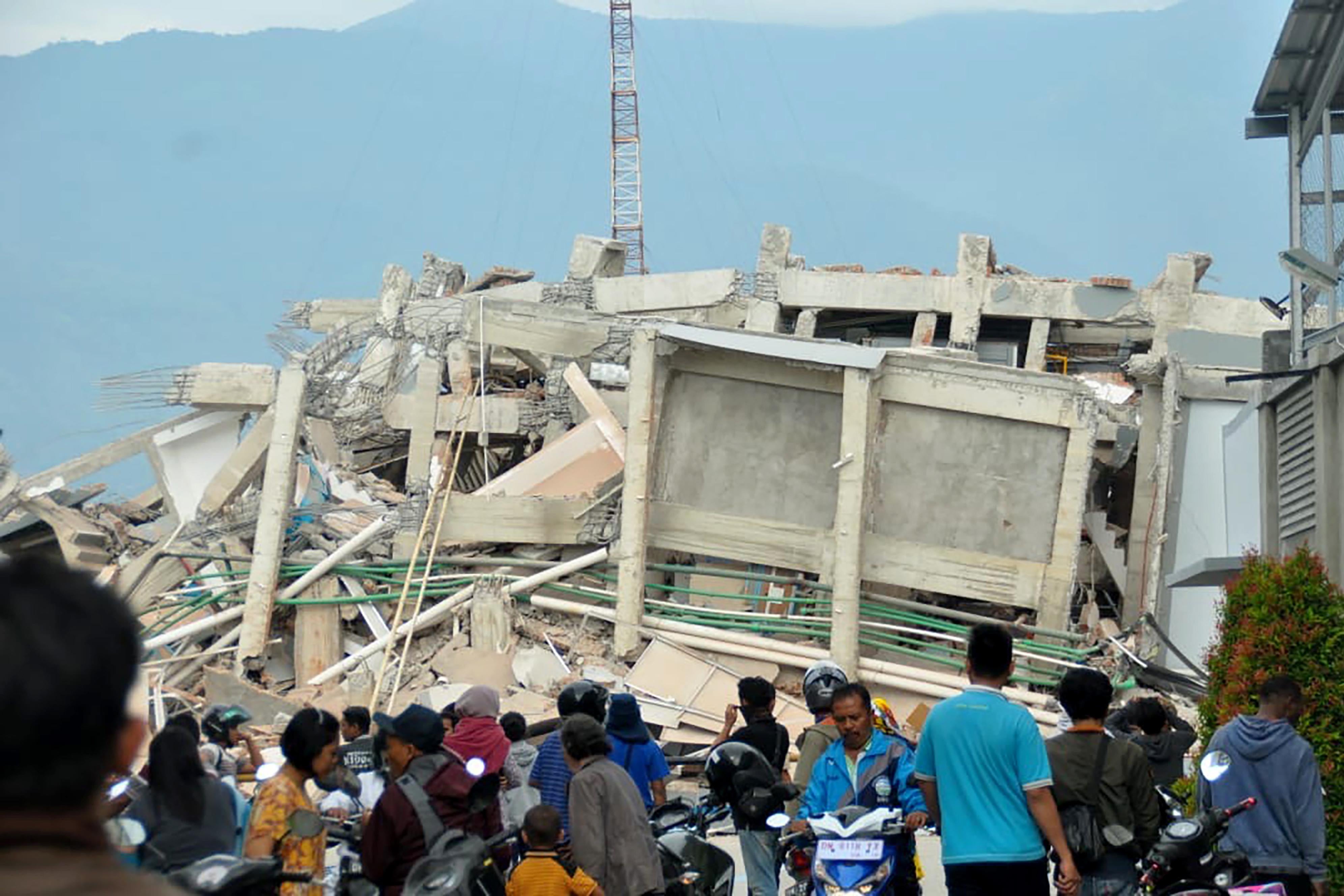 Residents gather to look at a collapsed building after an earthquake and tsunami hit Palu.