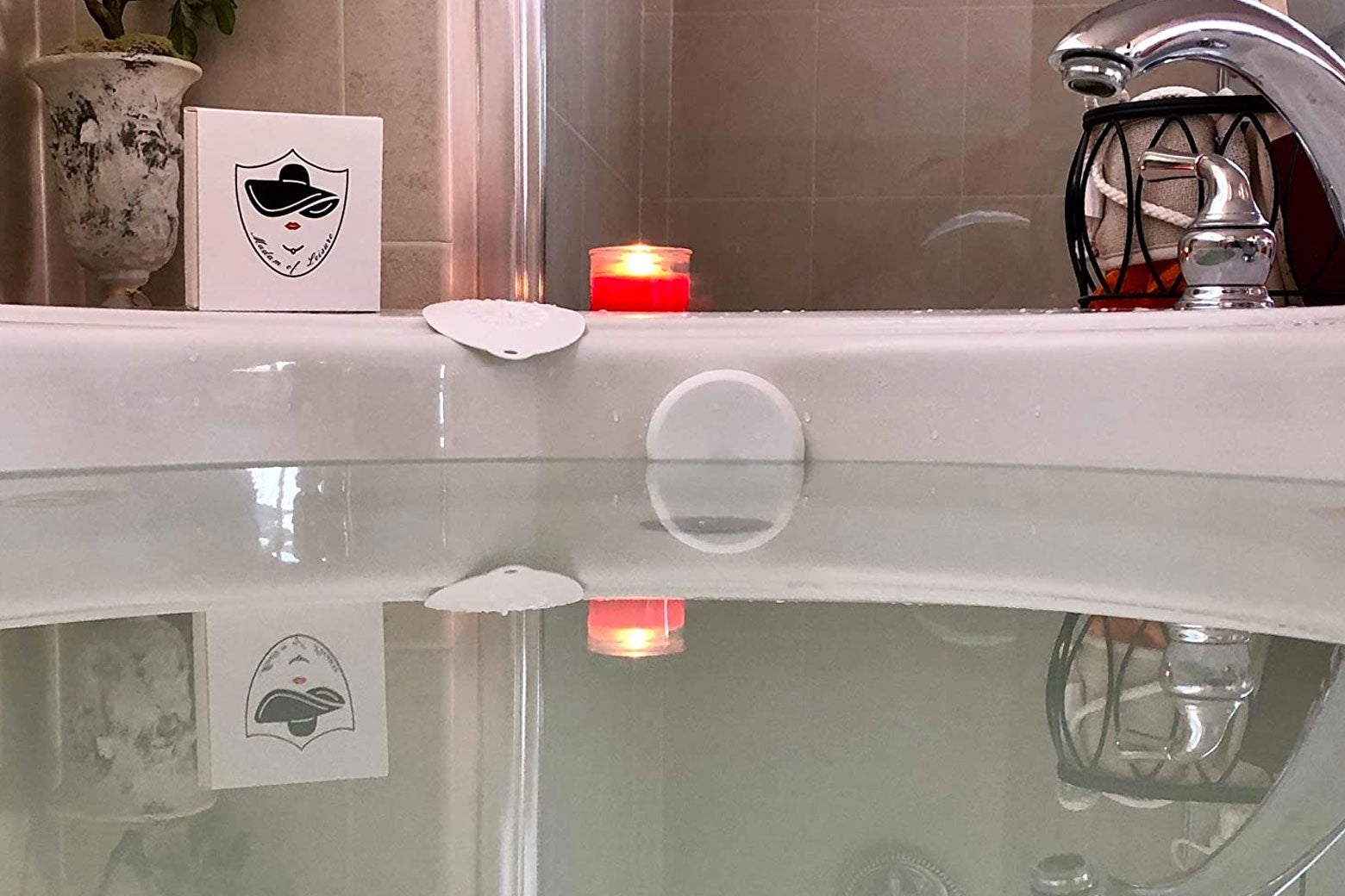 Bathtub full of water with overflow drain covered and a lit candle on the ledge