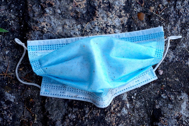 A blue surgical mask in the dirt.