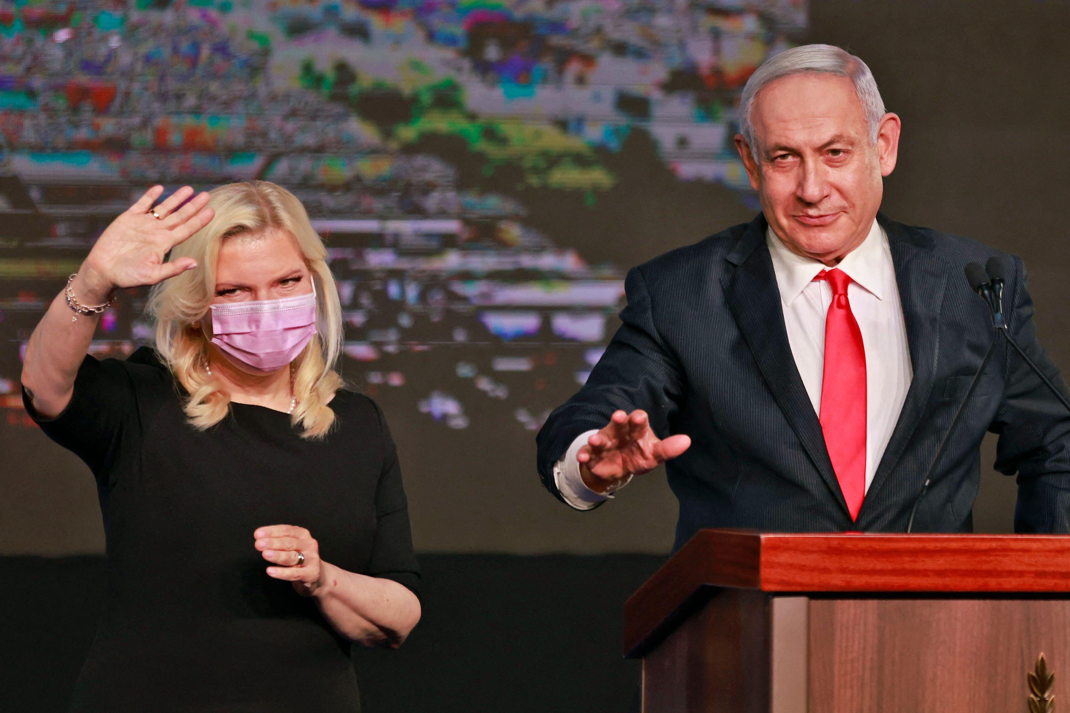 Sara waves to the crowd as she stands next to Benjamin Netanyahu, who is at a podium