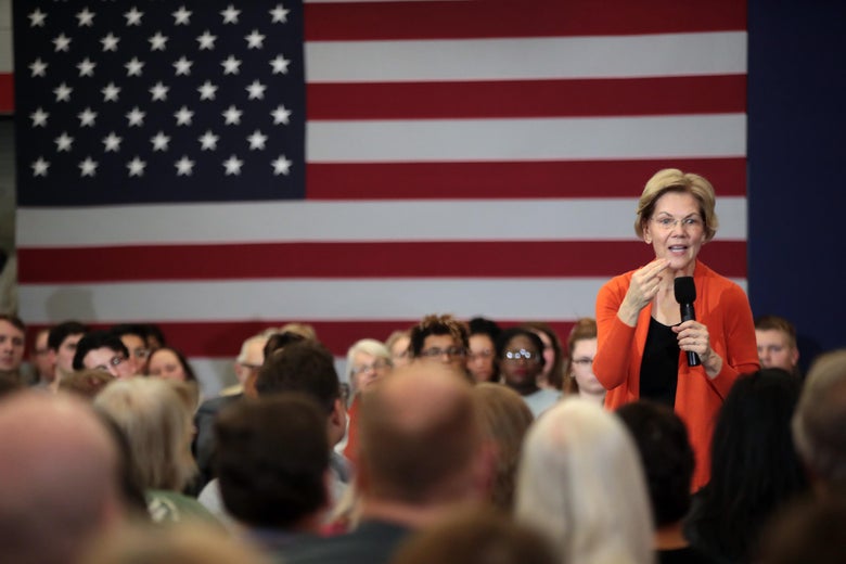 Elizabeth Warren speaks to a crowd, with an American flag in the background.