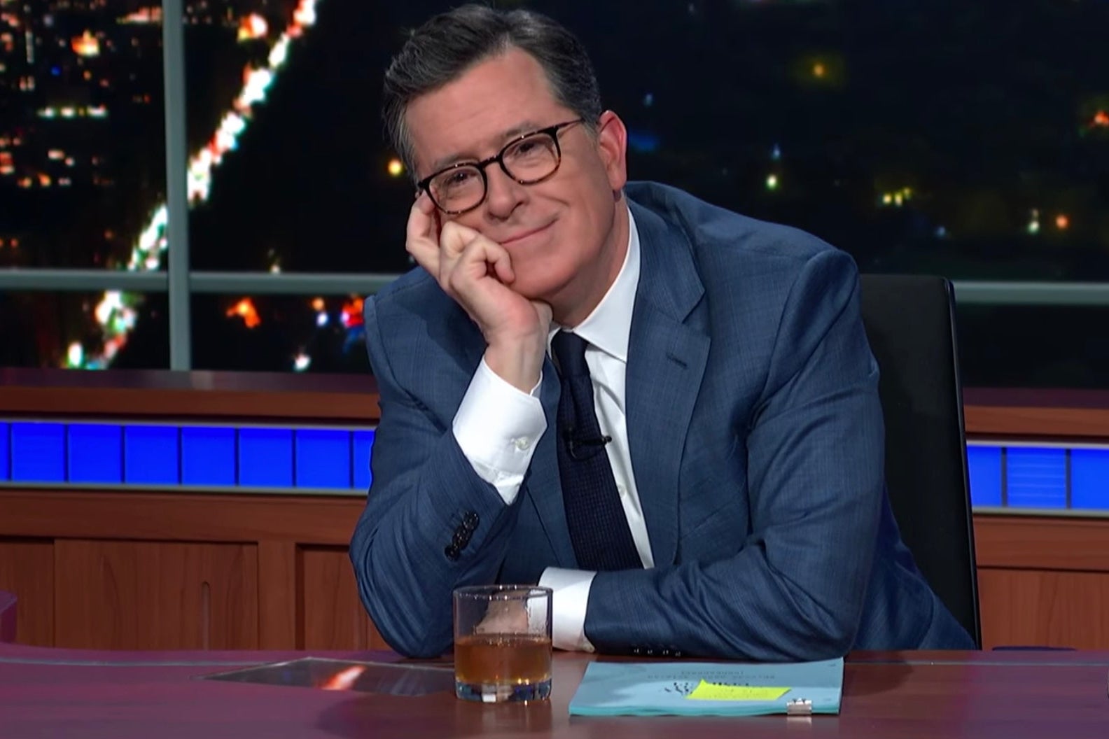 Stephen Colbert sits at his Late Show desk, a glass of Scotch and a script in front of him.