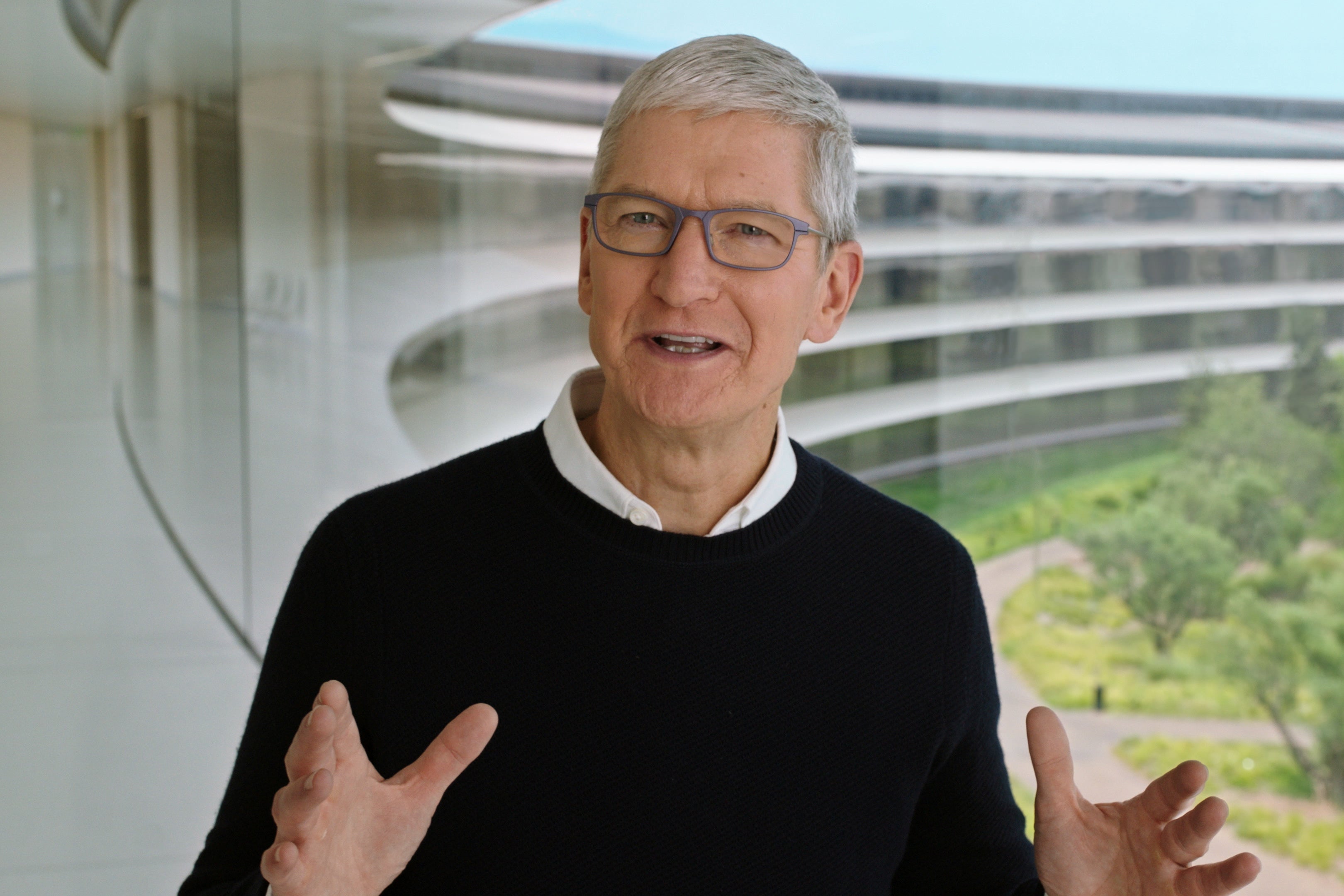 Tim Cook in front of a window showing trees and Apple's headquarters.