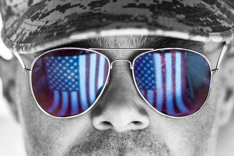 Close-up of a man in a camouflage cap wearing aviator sunglasses that show reflections of American flags
