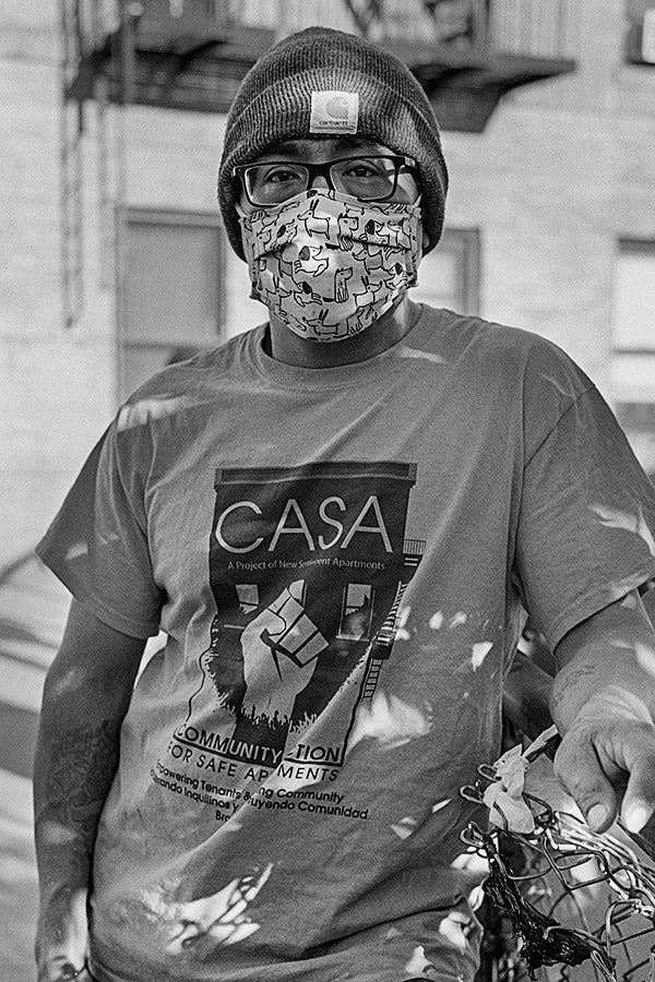 Andrés Vargas stands in front of a building wearing a beanie, a face mask, and a T-shirt reading CASA.