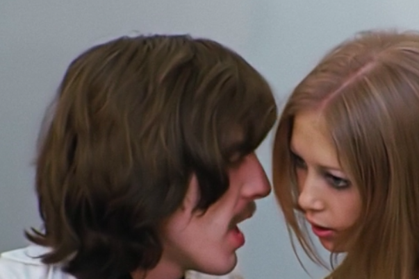A woman with long hair leans in close to George Harrison's face as he speaks