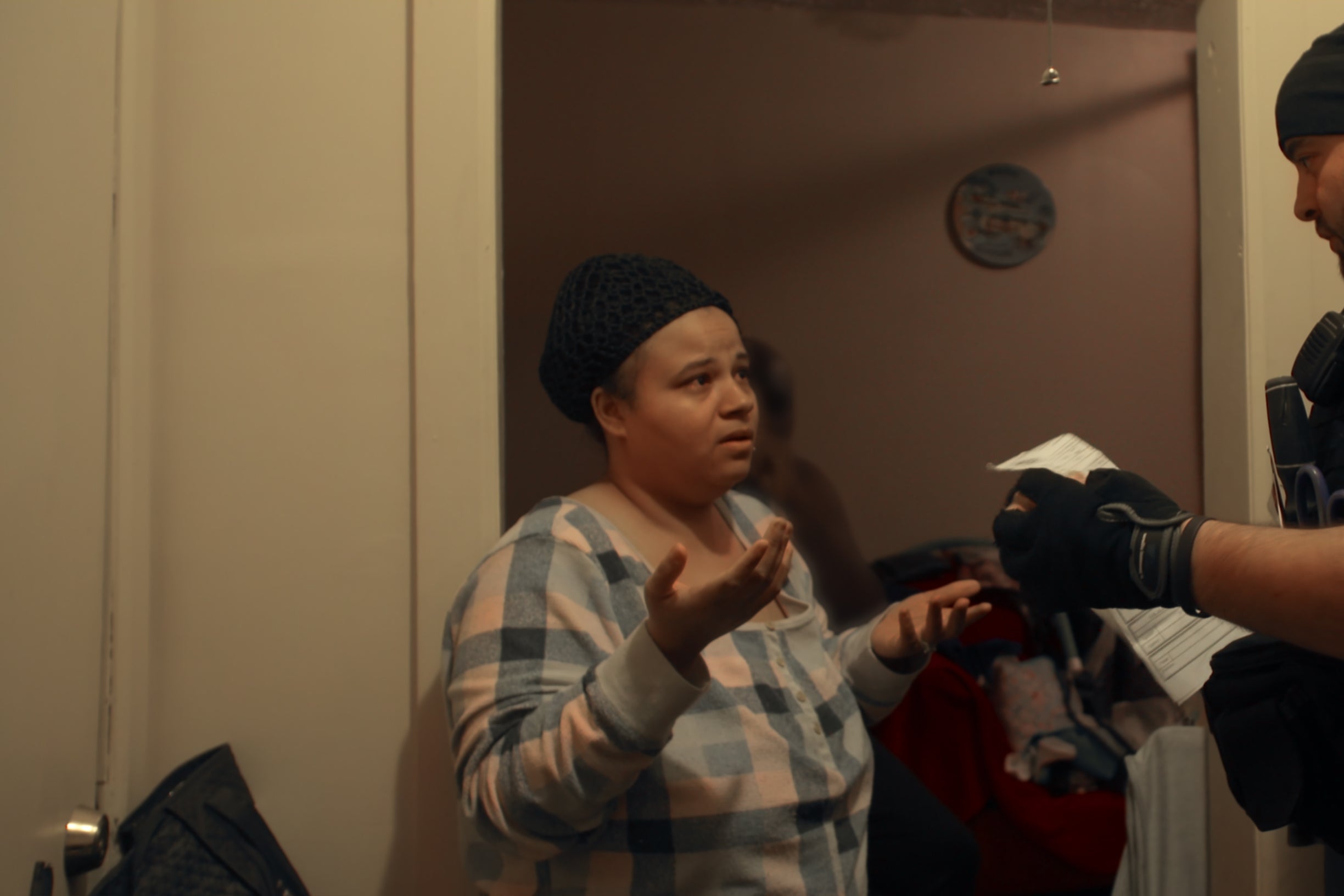 A uniformed man stands in front of a shrugging woman in a doorway.