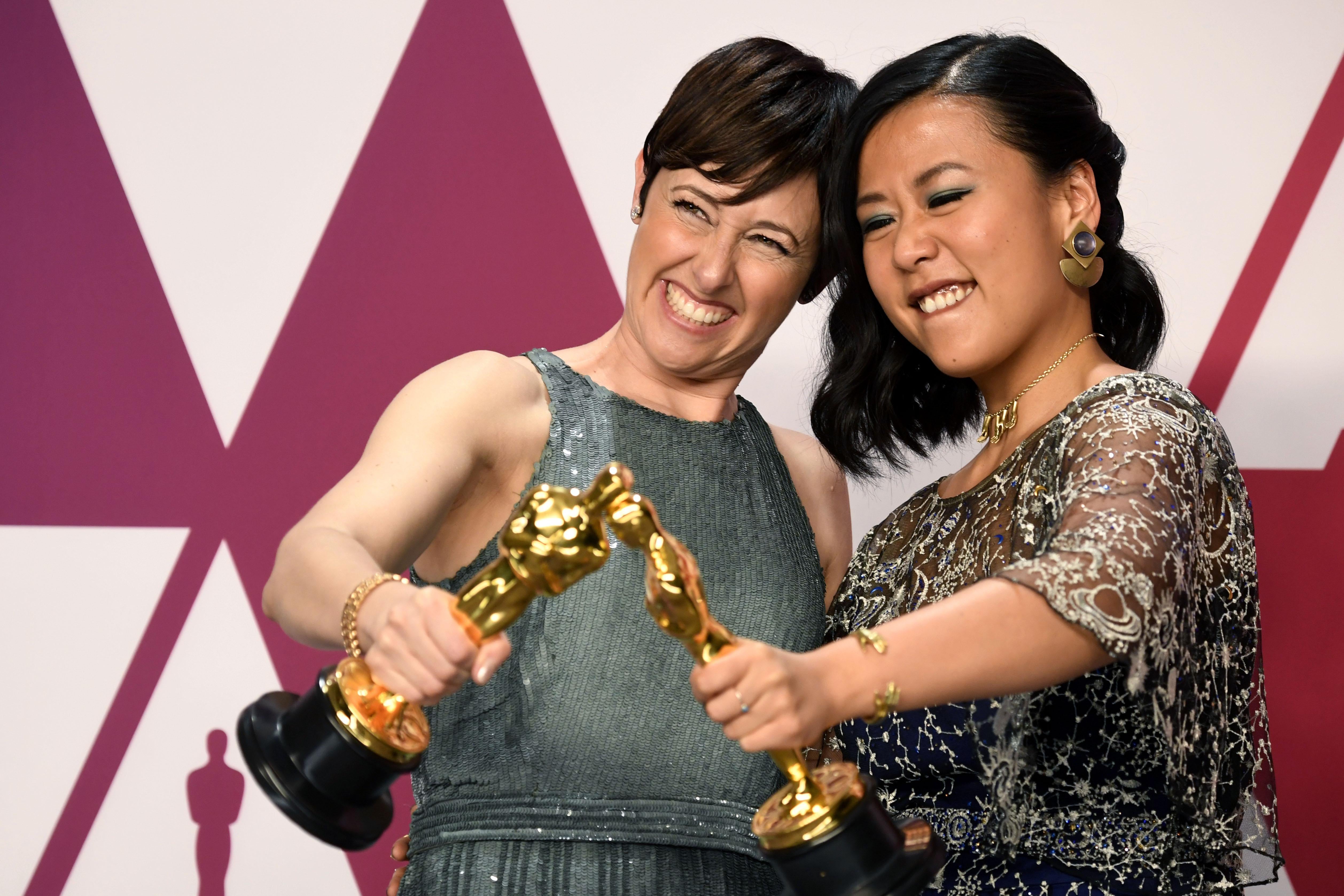 Two women hold Oscar statuettes.