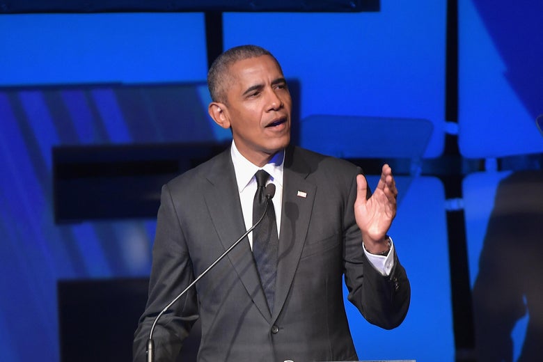 Barack Obama stands at a podium against a blue background.