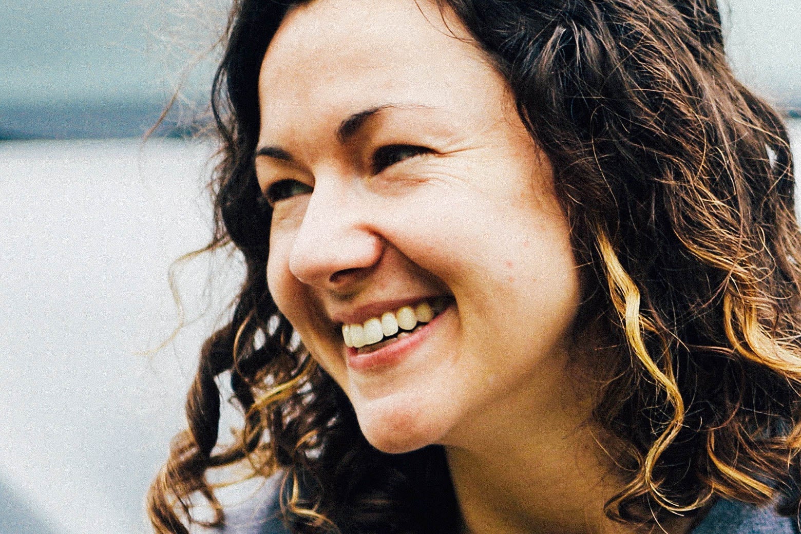 A woman with curly hair smiles as she looks off to the side.