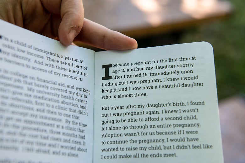 A hand holds up a booklet containing abortion stories.