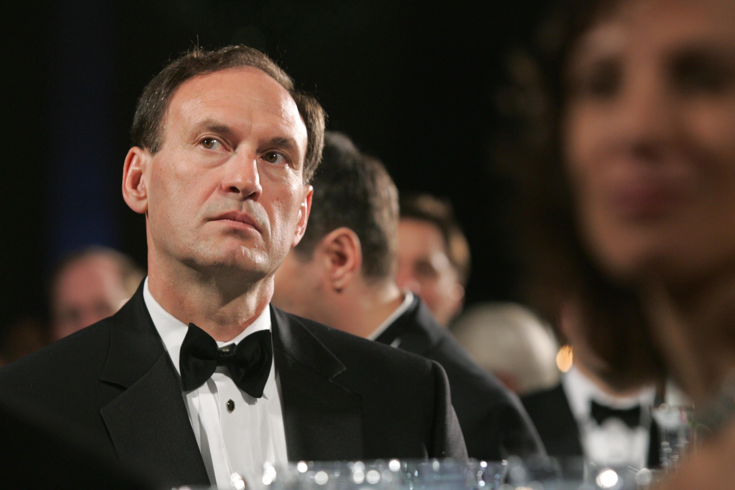 Alito in a tux looking up as he sits at a table at a fancy dinner