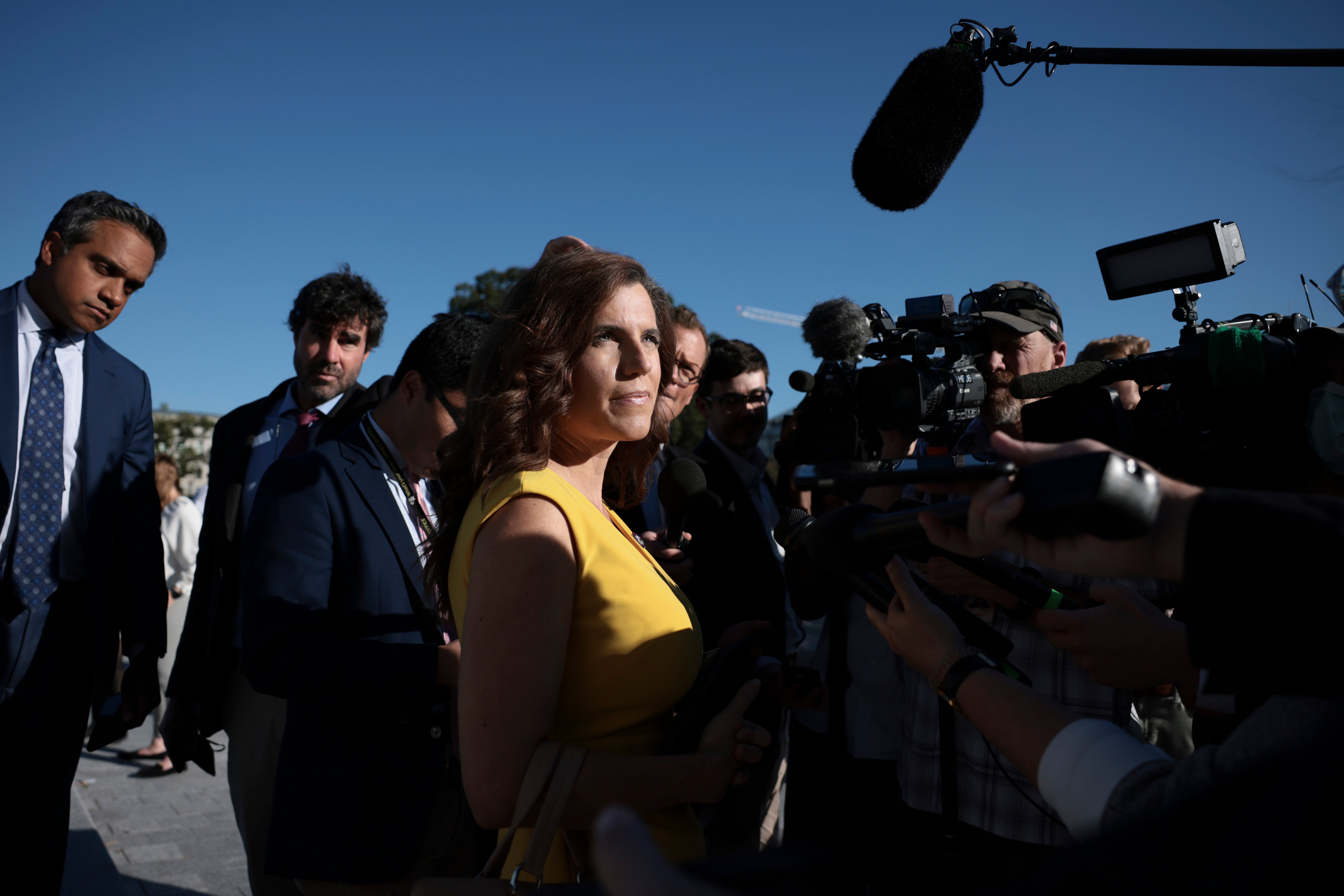 Mace, in a yellow dress, squints in the sun and talks to reporters.