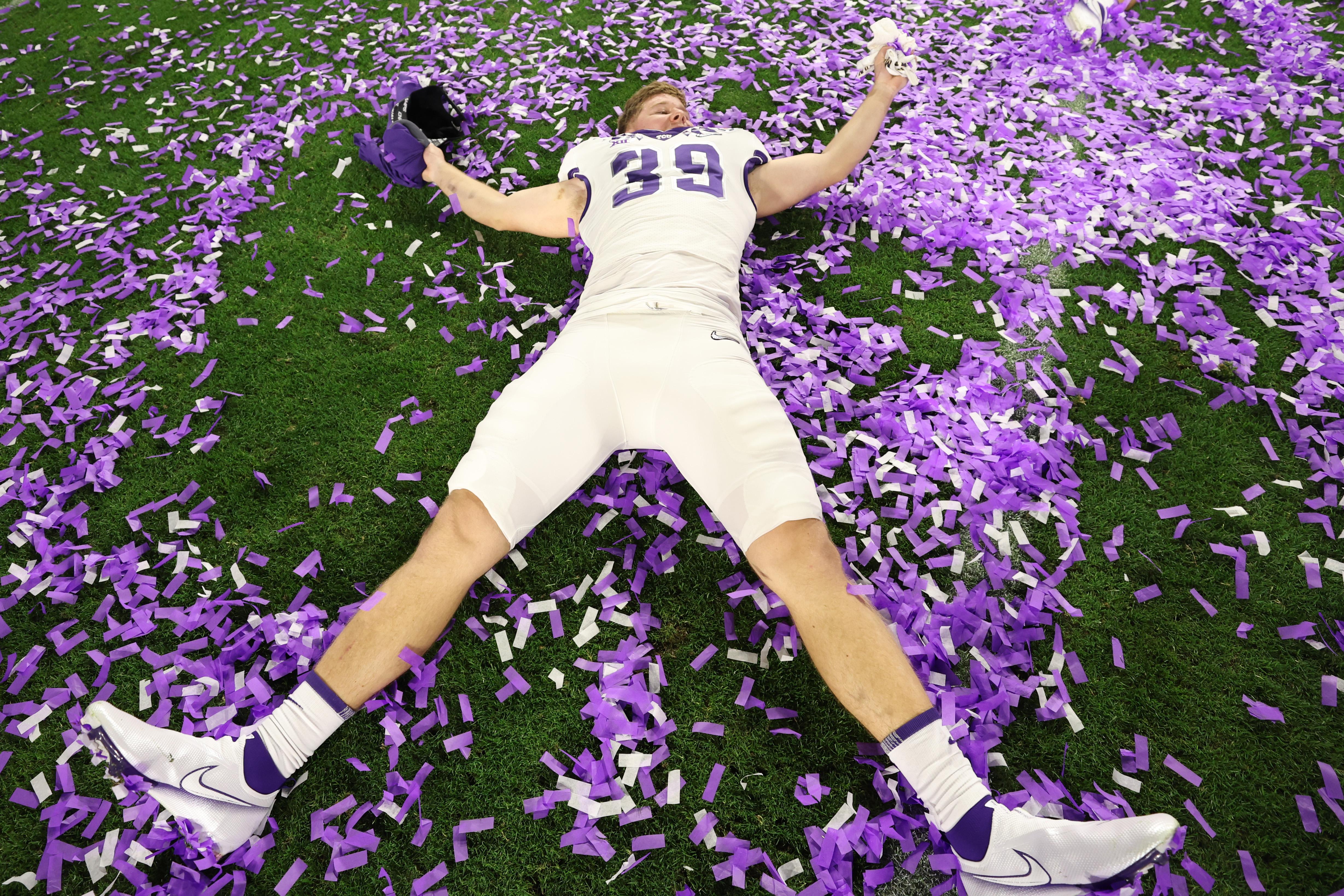 A TCU football player lies on his back and makes a "snow angel" in purple confetti. 