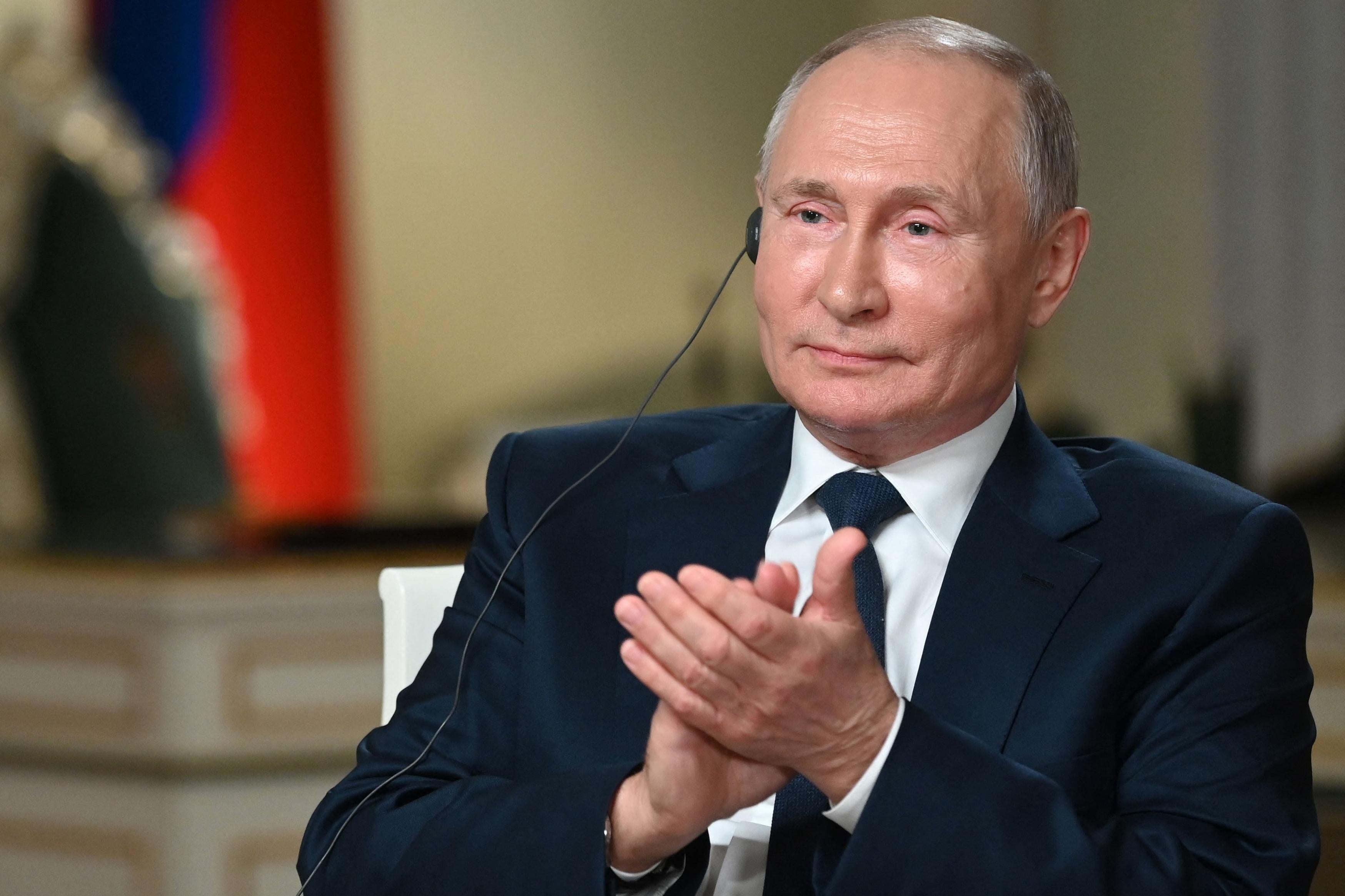 Putin holds his palms together as he wears an earpiece.