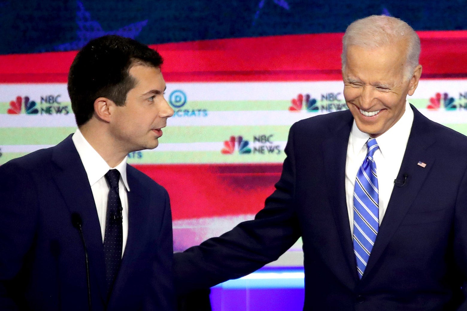 Joe Biden smiles and pats Pete Buttigieg on the back as they both stand on the debate stage.
