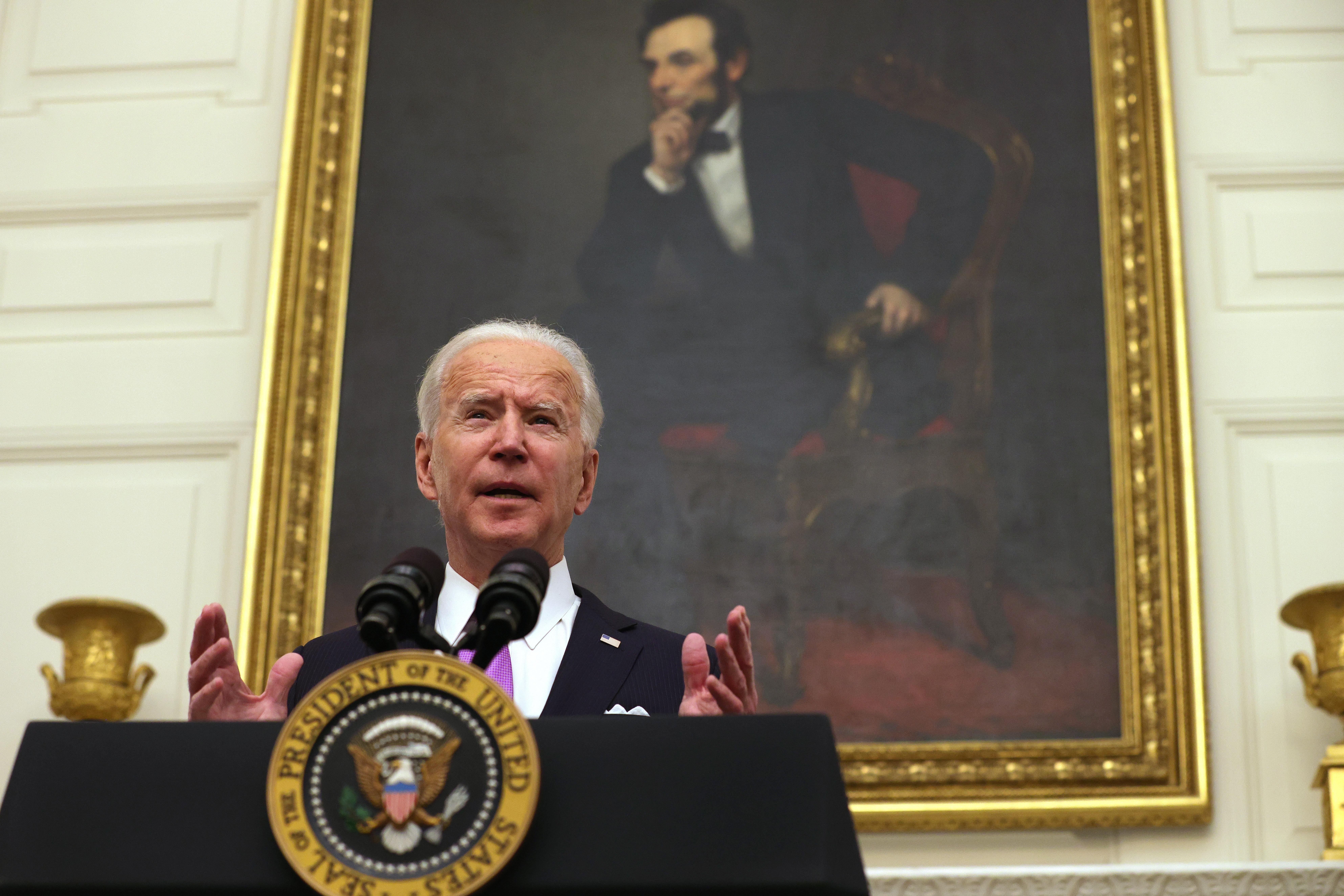 Biden speaks at a podium, standing in front of a portrait of Abraham Lincoln hanging in the State Dining Room