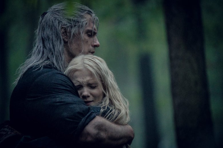 A long-haired man hugs a small blonde girl in the forest.