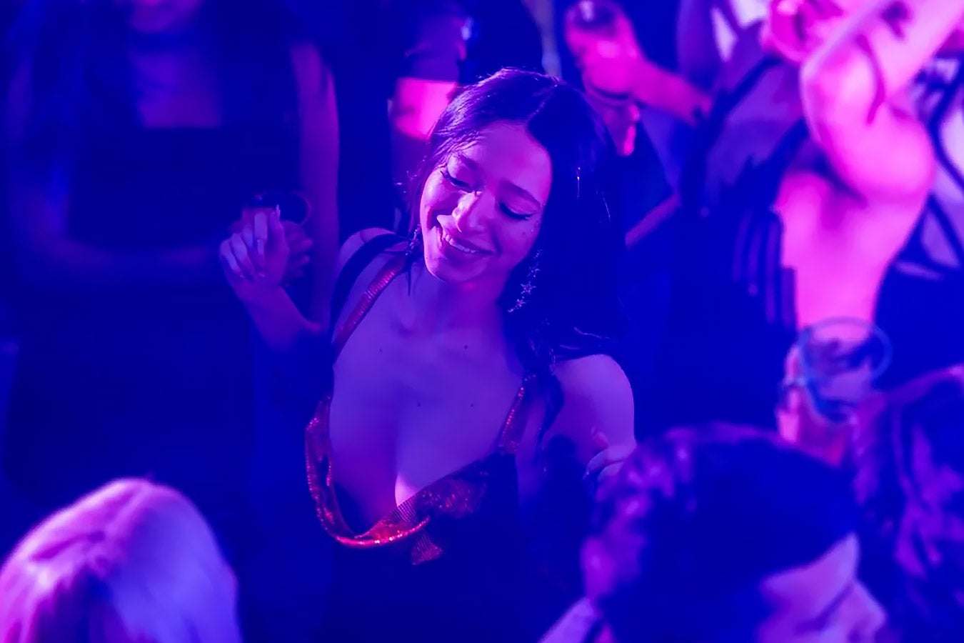 A pale white woman with dark hair dances in a violet-hued club.