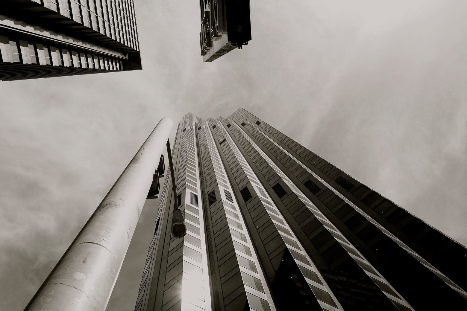 A black-and-white photo, taken from the ground and looking nearly straight up, of a 50-story-ish glass and steel office building.