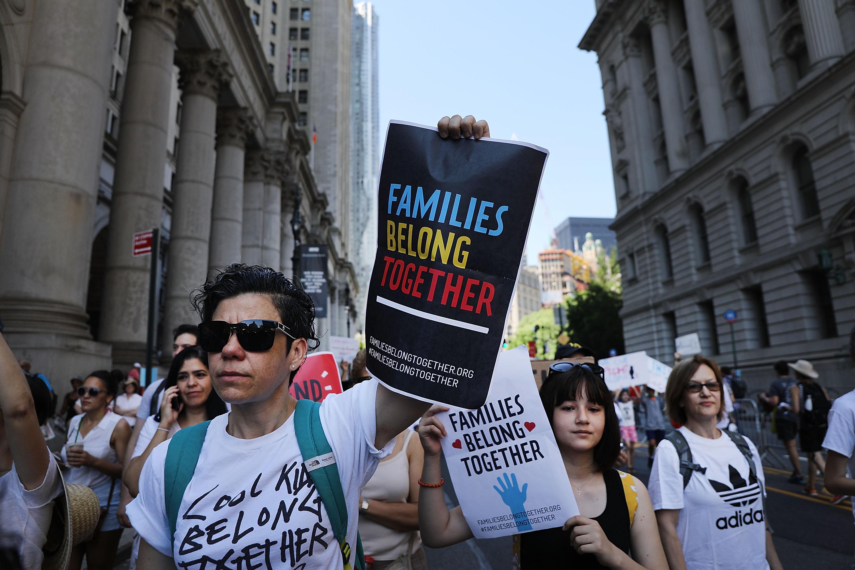 A man holding a sign that says "families belong together" leads a march of protesters with similar signs.