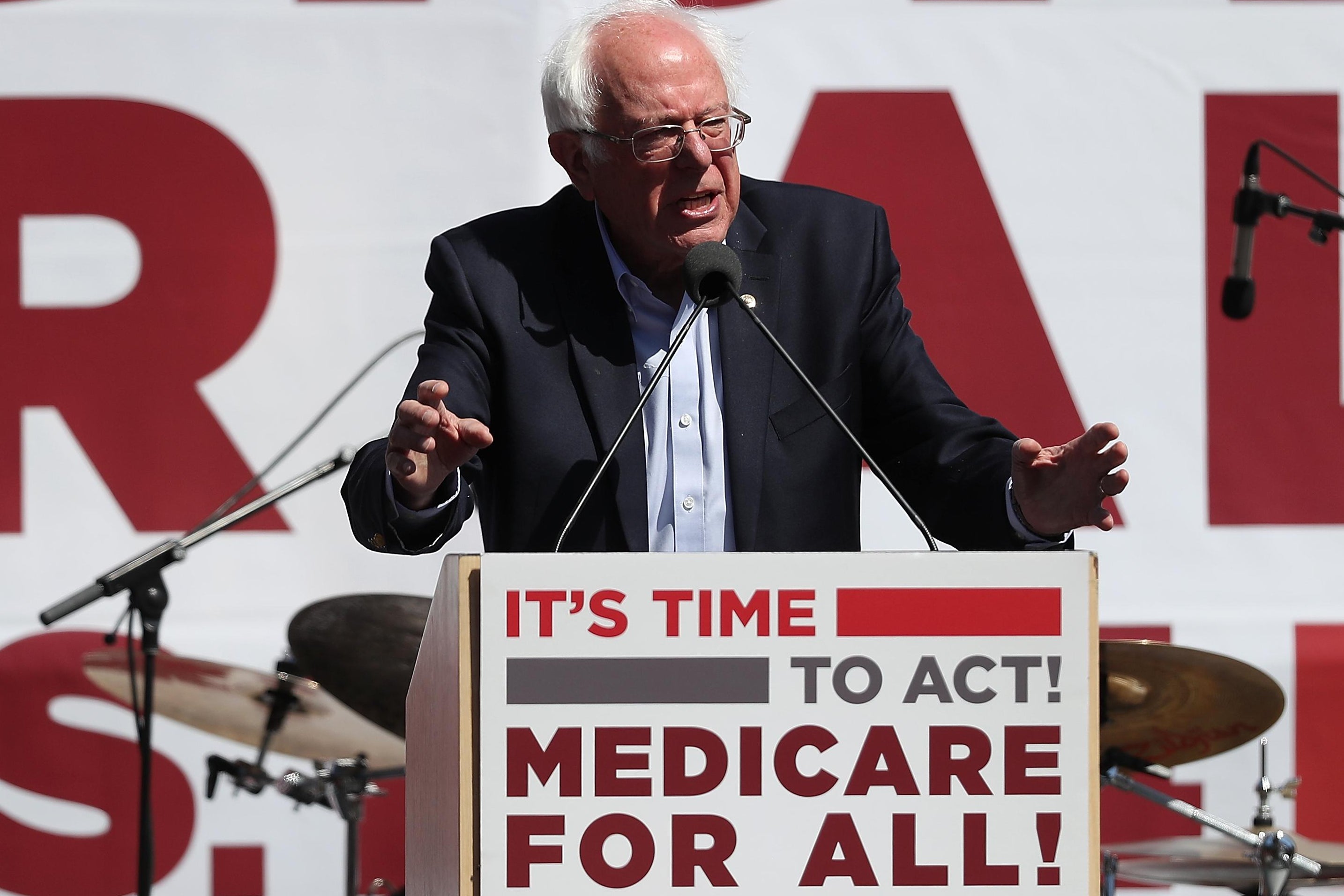 Bernie Sanders speaks from a podium that says "It's time to act! Medicare for all!"