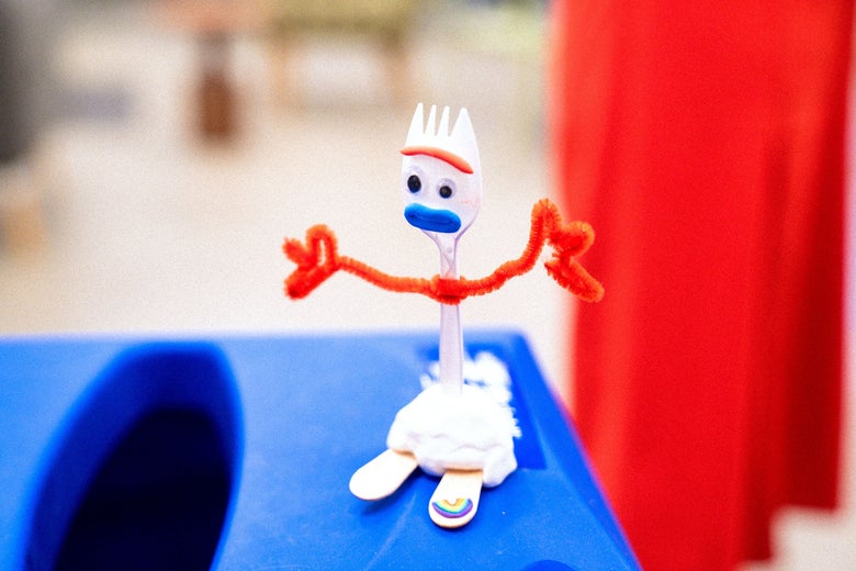A homemade Forky stands on a blue trash can.