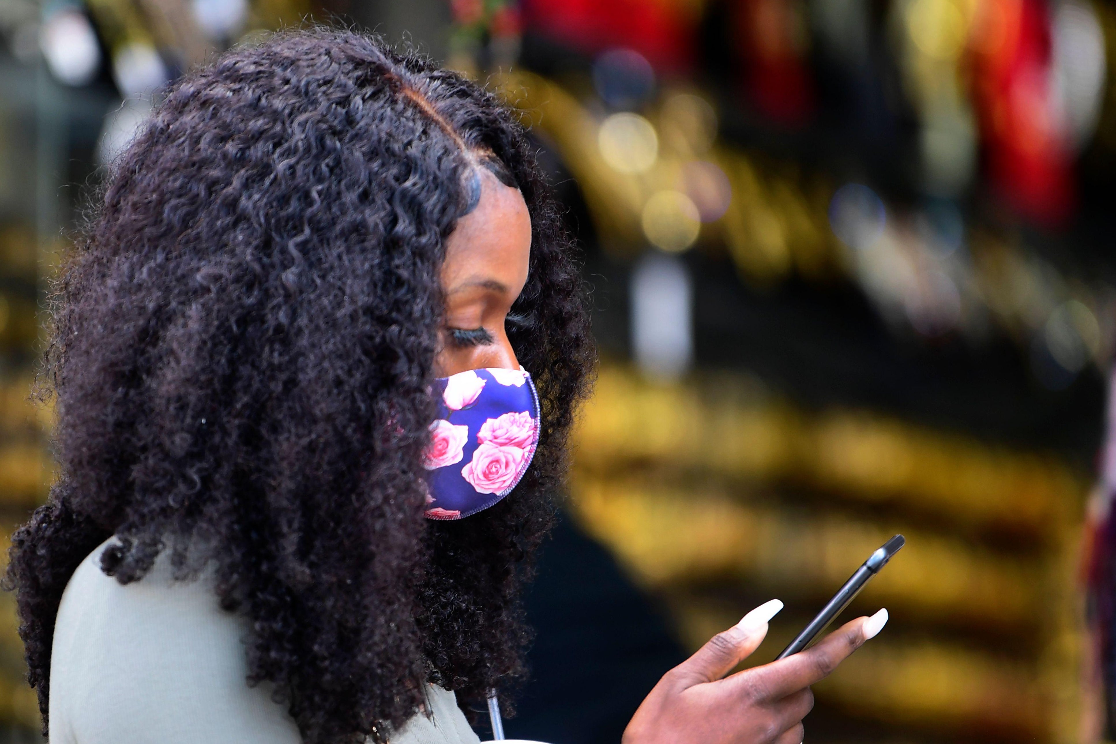A woman wearing a cloth face mask with flowers checks her cellphone.