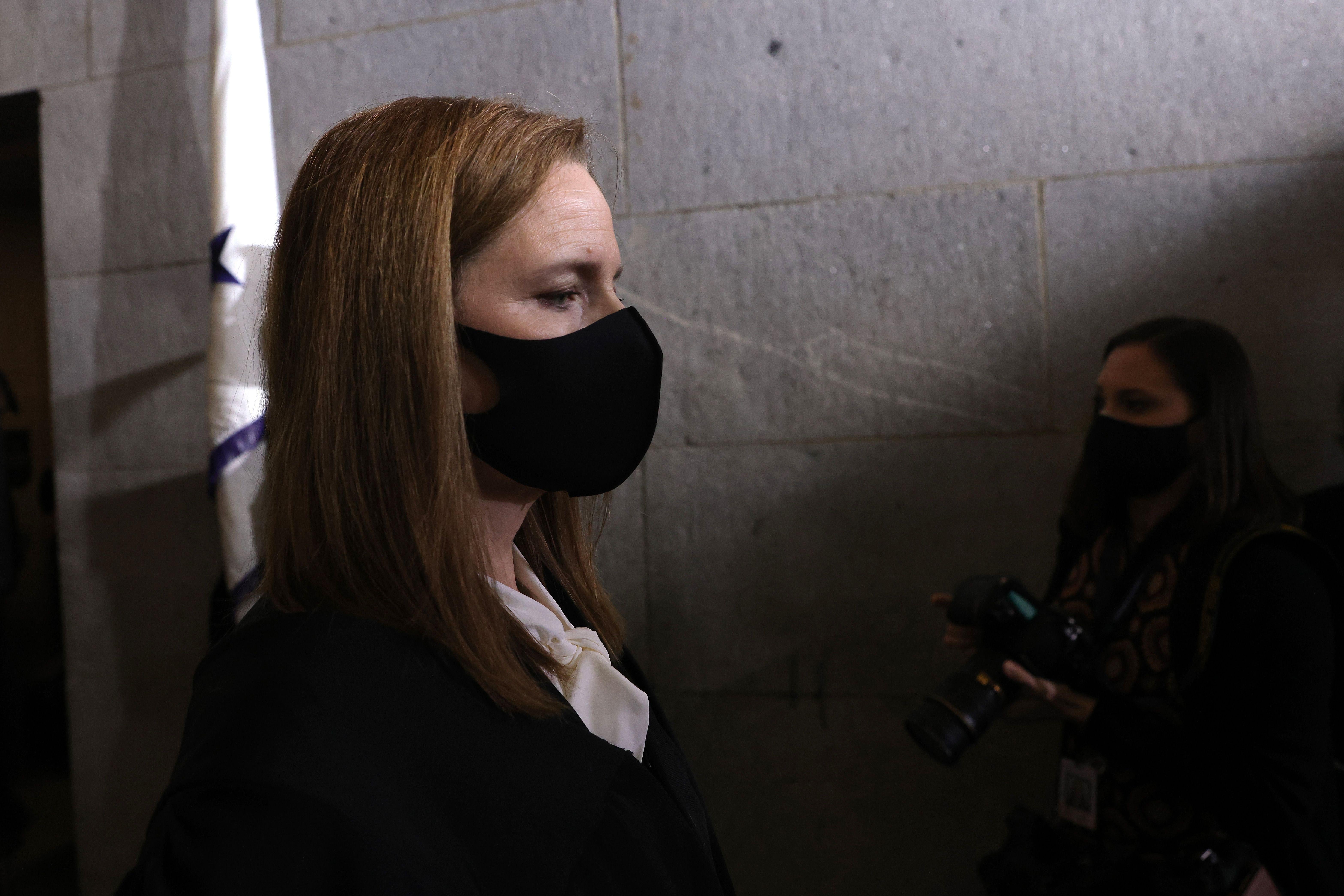 Amy Coney Barrett stands in a dark hallway wearing a black mask