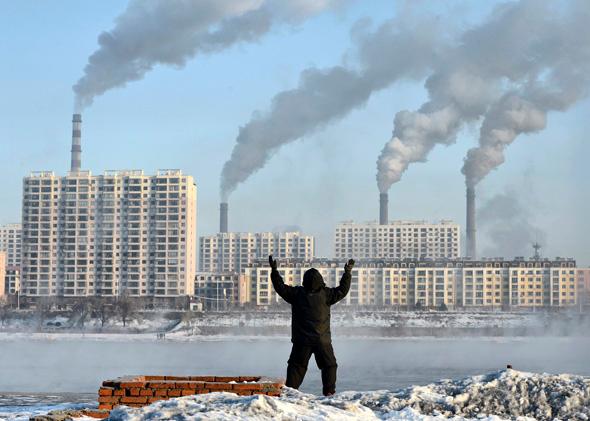 An elderly man exercises in the morning as he faces chimneys emitting smoke behind buildings across the Songhua river in Jilin.