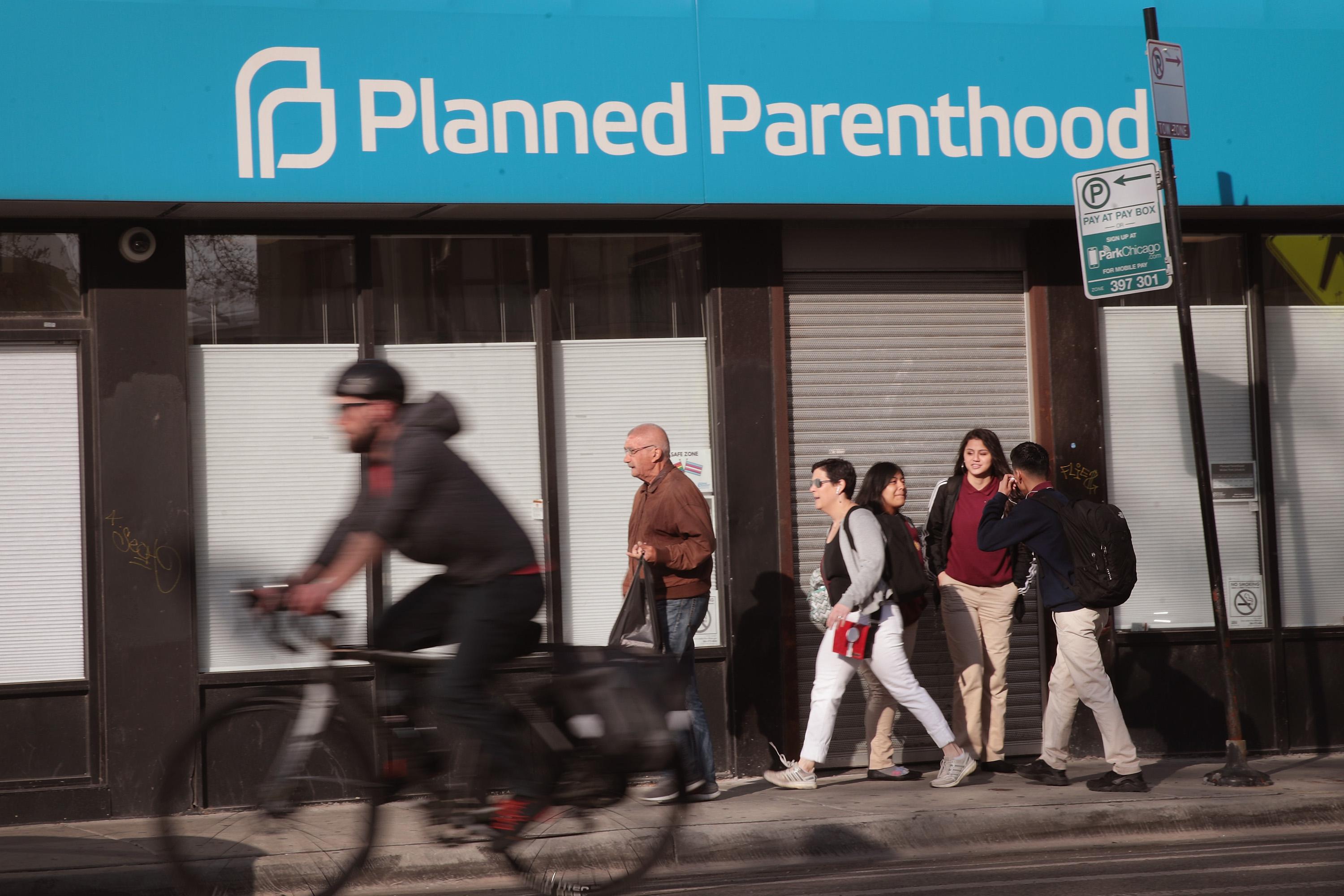 Pedestrians and a cyclist move past a Planned Parenthood awning on a building.