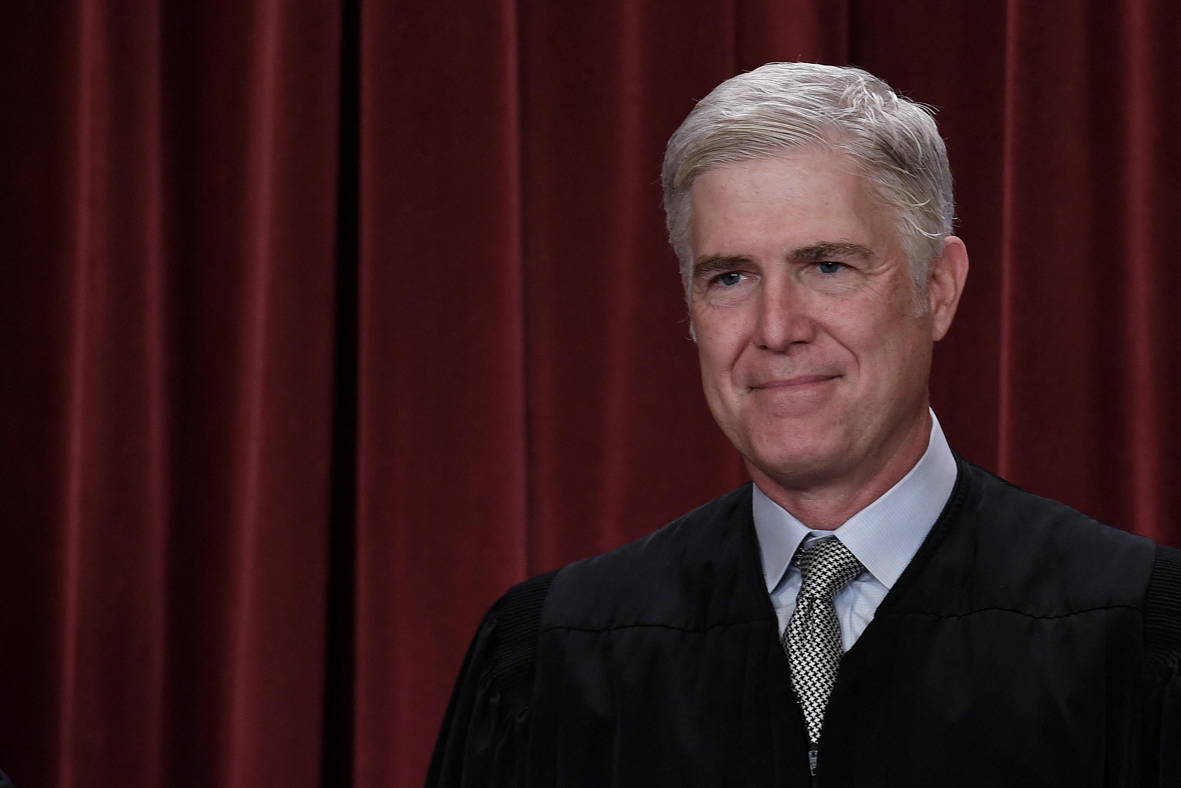 Justice Neil Gorsuch in his robe in front of a red curtain