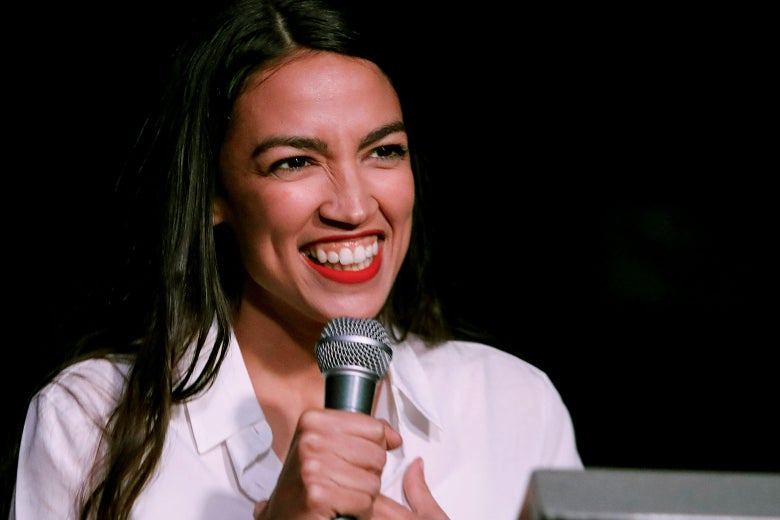 Ocasio-Cortez holding a mic and smiling.