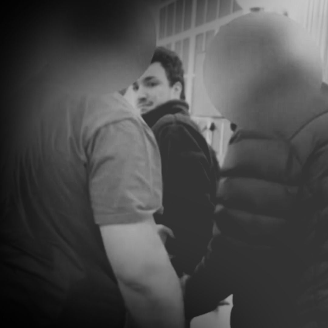 Black-and-white image of a young man with dark hair, blurred in the background of a jail cell, behind federal agents.