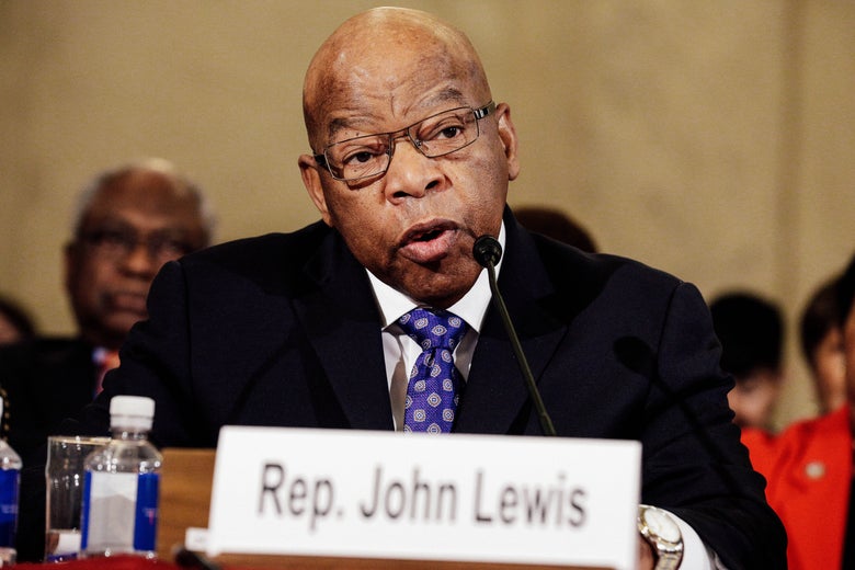 John Lewis speaks at a microphone, with a sign featuring his name displayed in front of him.