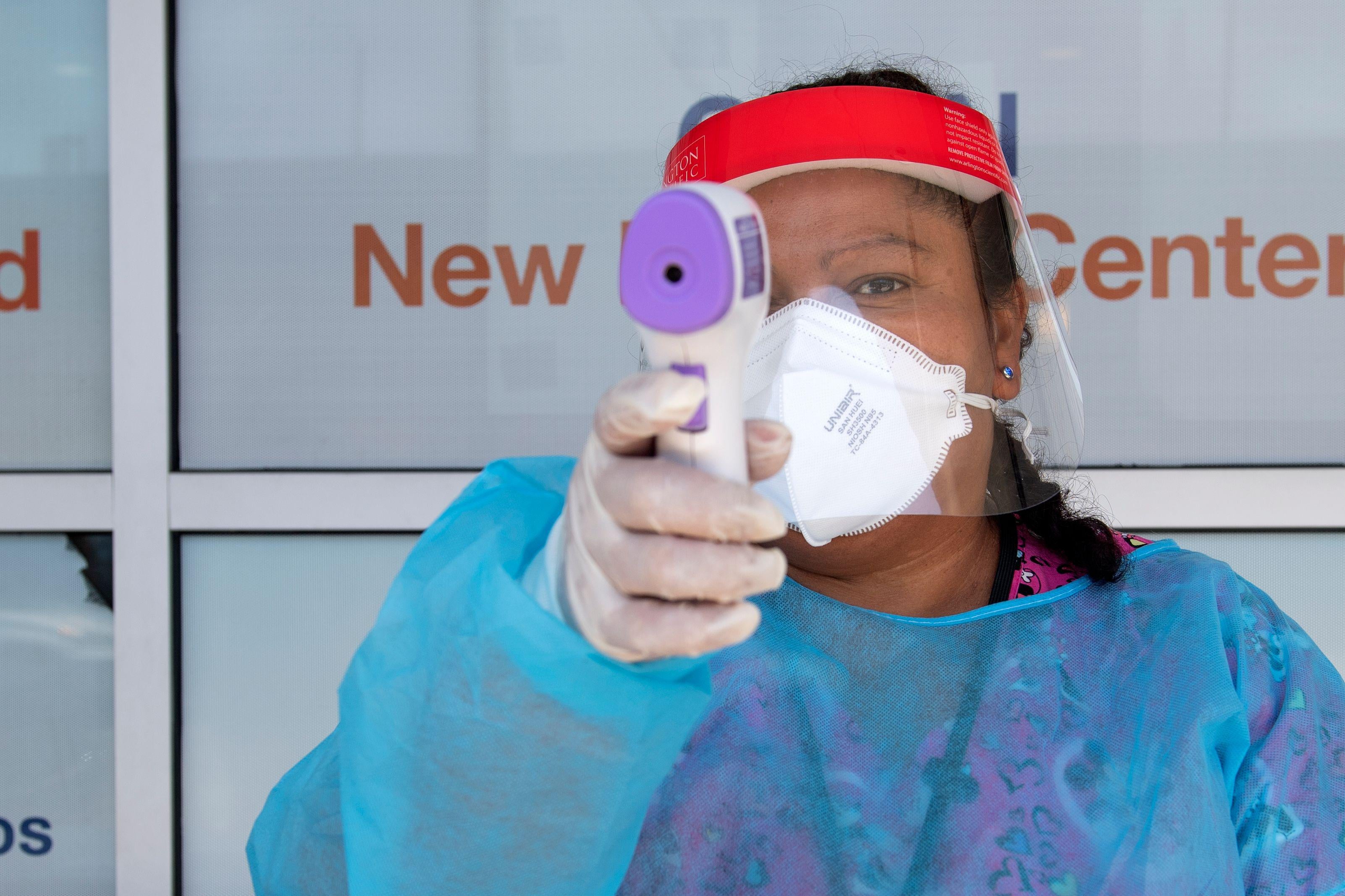 A health worker dressed in personal protective equipment points a thermometer at the camera. 