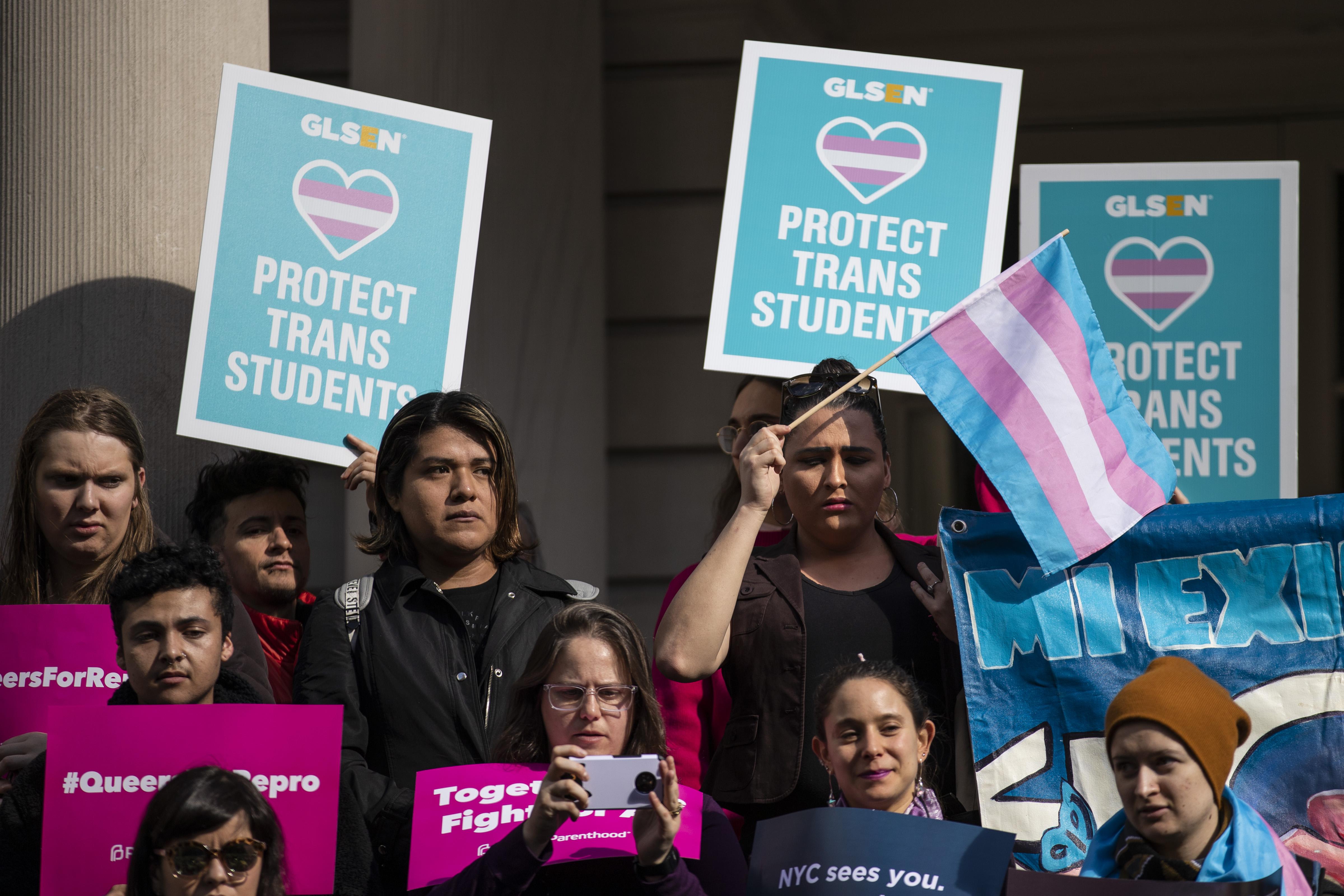 LGBTQ activists hold up signs supporting trans students