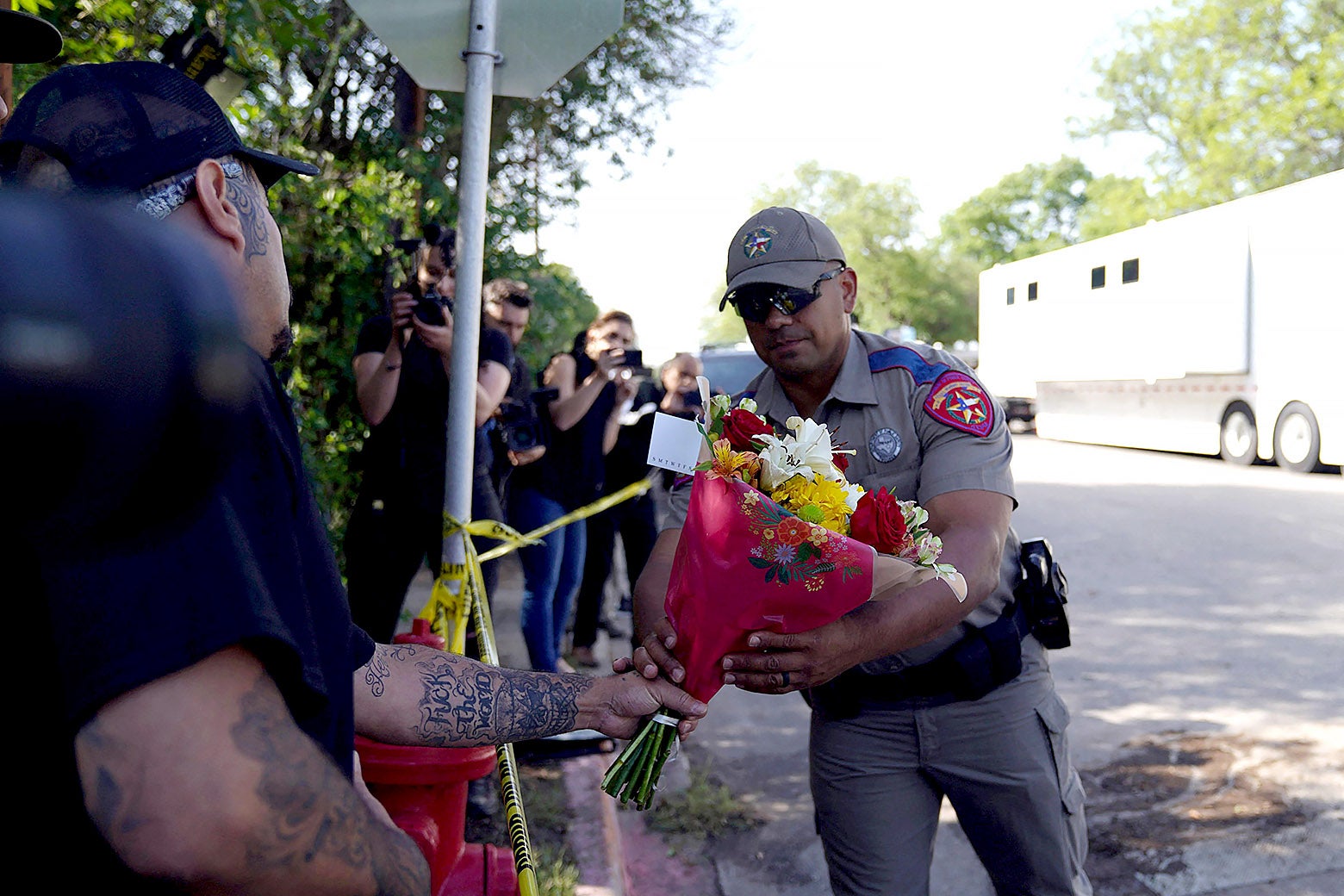 A police officer takes flowers for the memorial from a person standing behind yellow police tape.