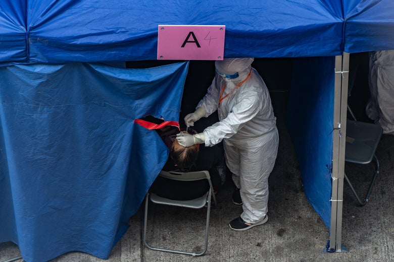 A health worker in full protective gear administers a coronavirus swab in a patient’s nose in a makeshift tent.