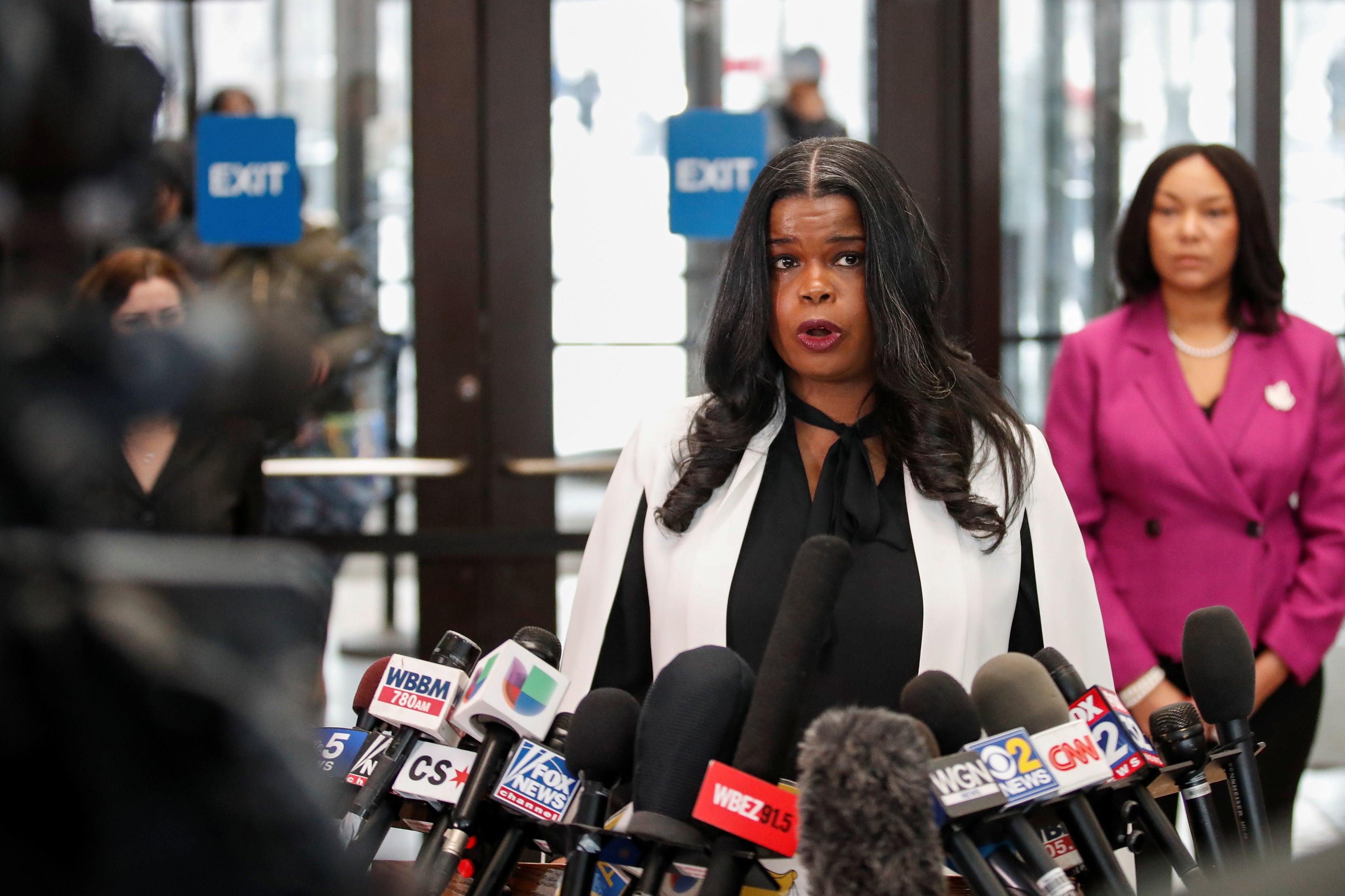 Foxx speaking at a cluster of microphones in front of a courthouse