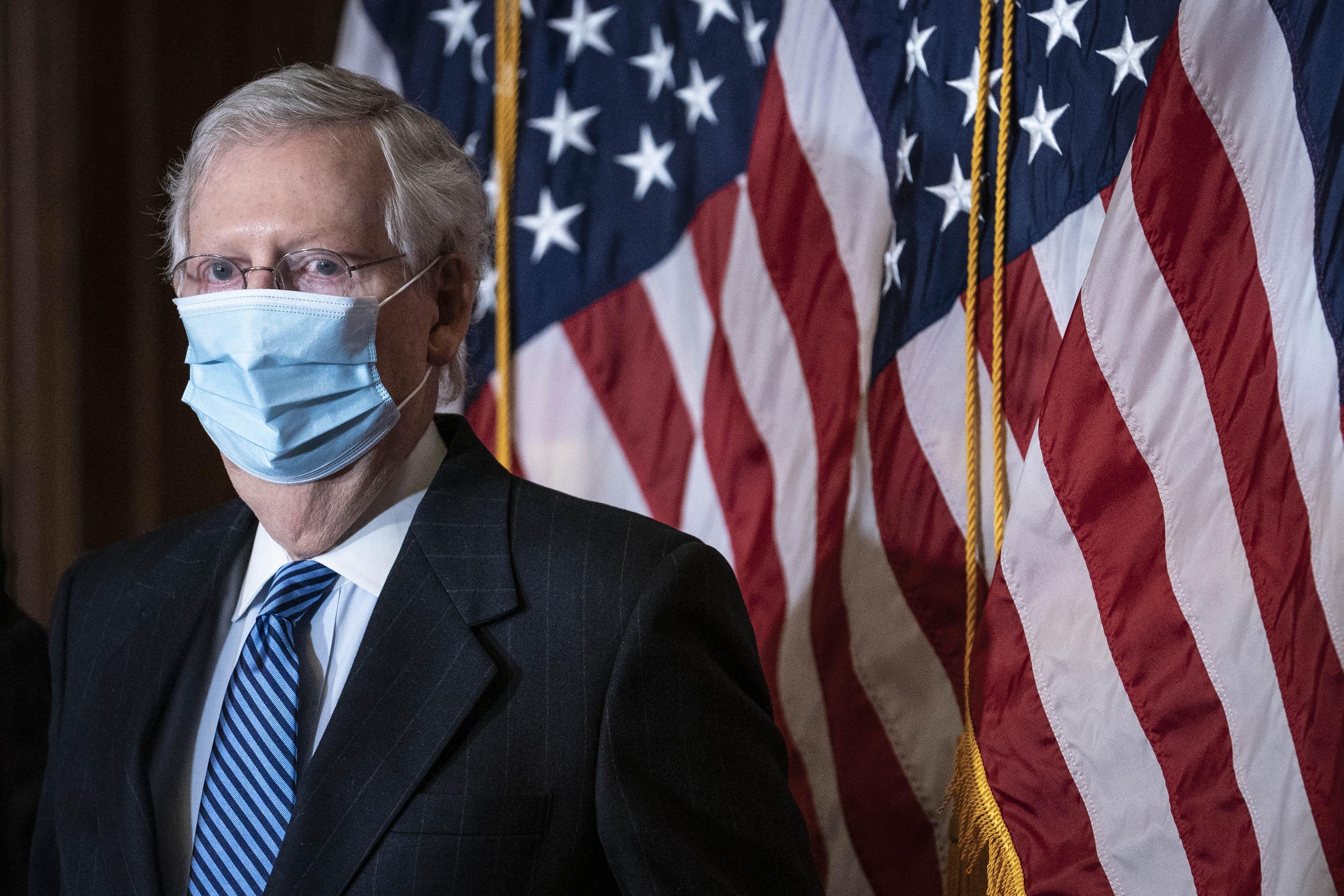 Mitch McConnell is seen wearing a face mask while standing front of U.S. flags.