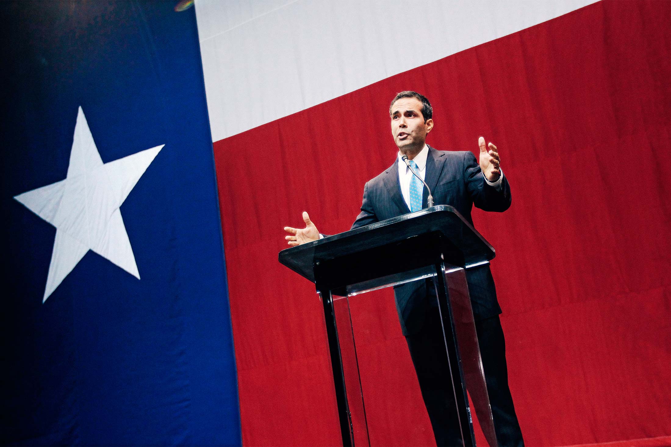 George P. Bush stands at a podium in front of a Texas flag.